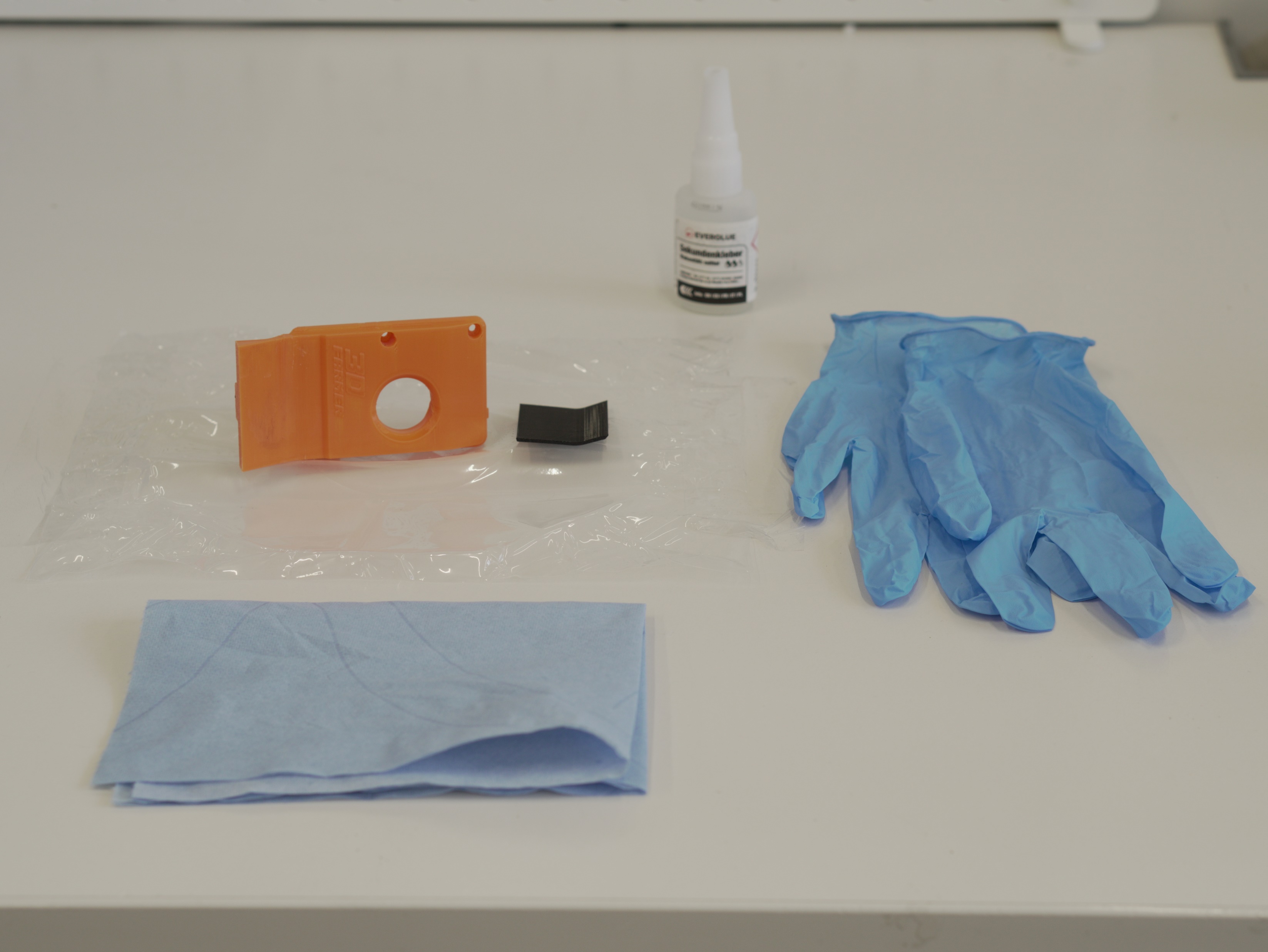 Scraper parts laid out: orange PETG scraper, black TPU piece, glue, gloves, paper towel